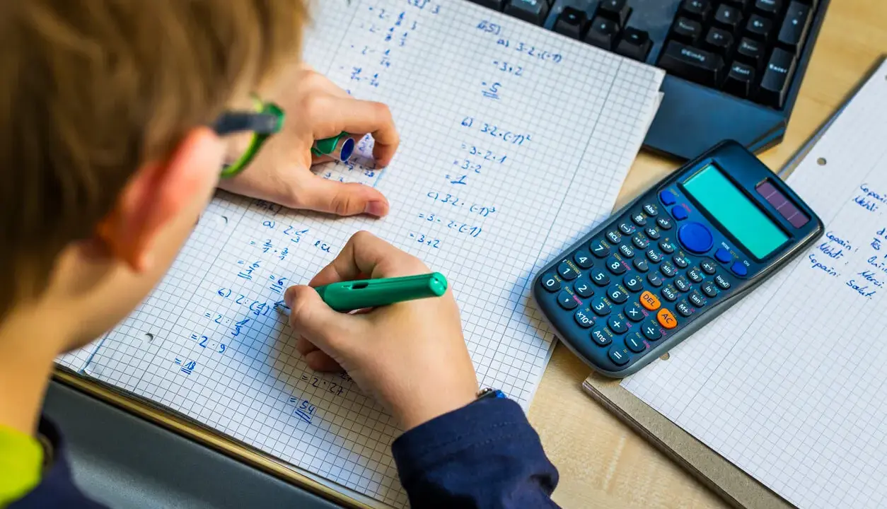 Niño resolviendo problemas matemáticos, practicando la tabla del 7. Una calculadora y un teclado están cerca.