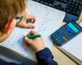 Niño resolviendo problemas matemáticos, practicando la tabla del 7. Una calculadora y un teclado están cerca.