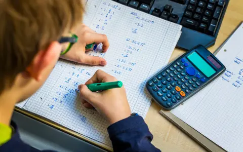 Niño resolviendo problemas matemáticos, practicando la tabla del 7. Una calculadora y un teclado están cerca.