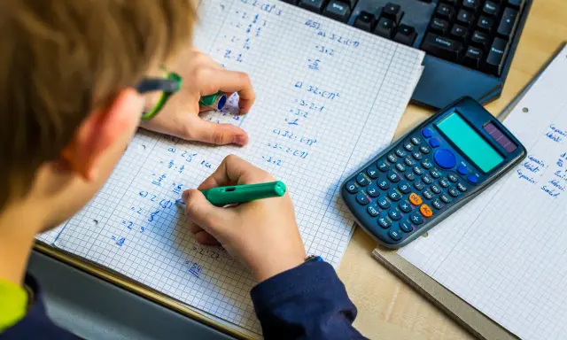 Niño resolviendo problemas matemáticos, practicando la tabla del 7. Una calculadora y un teclado están cerca.